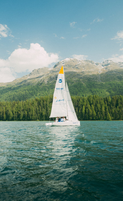 Segelboot im Sommer auf einem See, im Hintergrund sommerliche Berglandschaft.