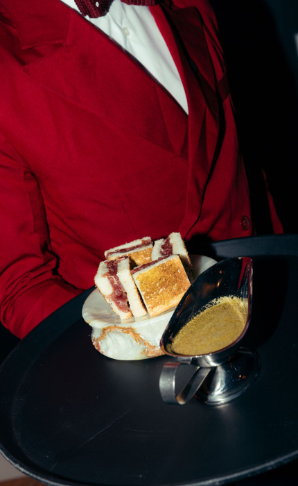Serviceangestellte in roter Uniform, serviert ein Gericht mit einer Sauce auf einem Tablett.